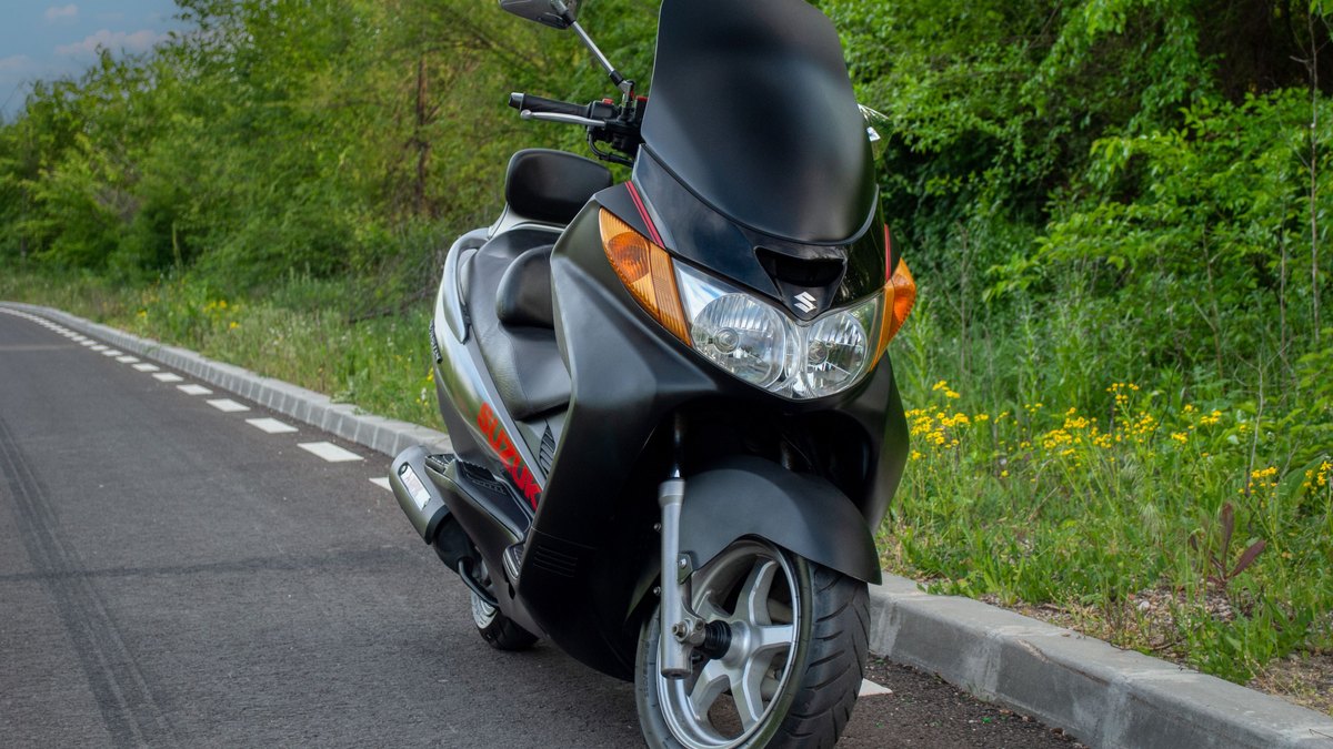 Scooter Suzuki noir stationné au bord d'une route bordée d'arbres pour illustrer le budget d'assurance scooter